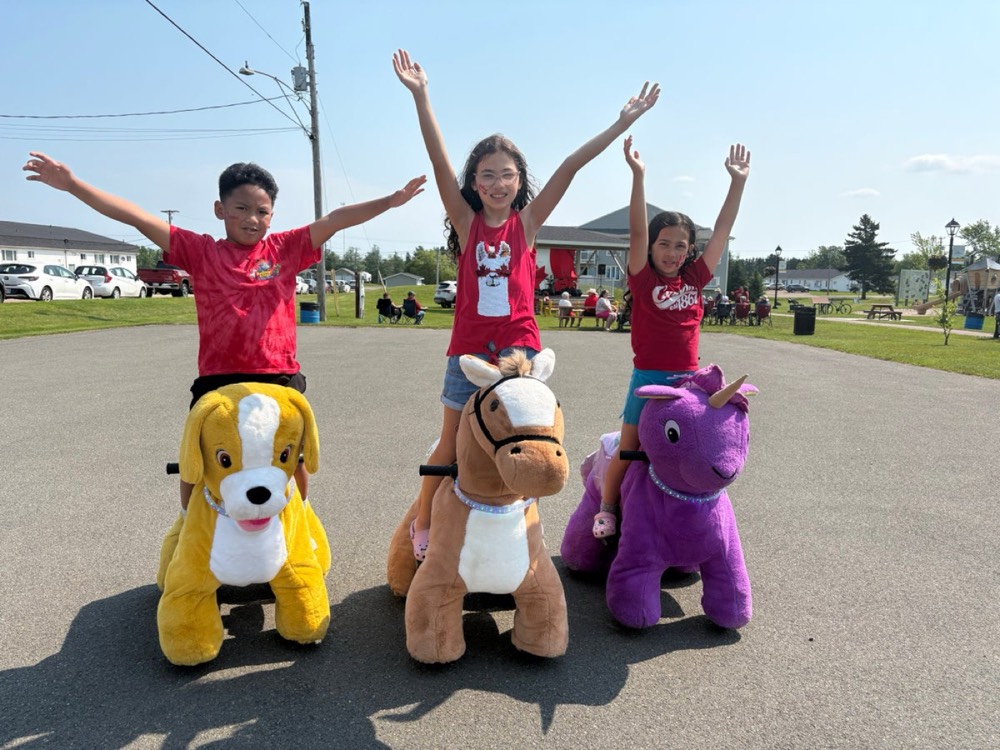 Three kids cheering beside a dog, horse and purple pony ride-on